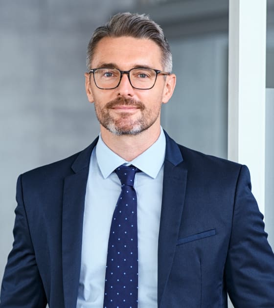 Man in suit with glasses, smiling confidently.